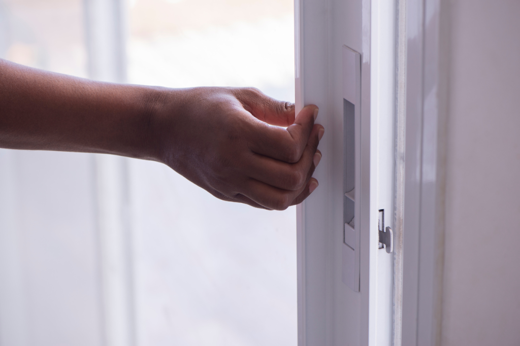person coming through sliding glass door with vertical blinds